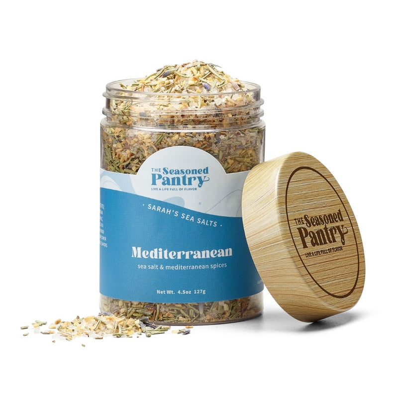 A clear glass jar with a wooden lid containing medium grain Mediterranean sea salt spiced with various herbs and spices.